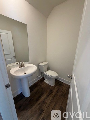A white bathroom with wood flooring and a white toilet.