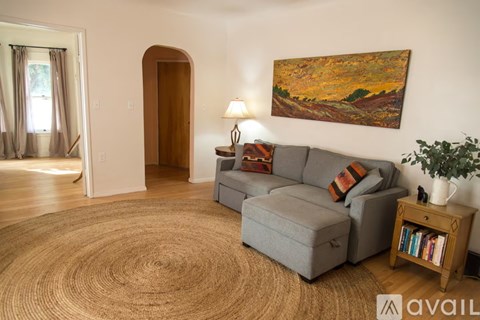 A living room with a grey couch, a brown rug, a wooden side table, and a painting on the wall.