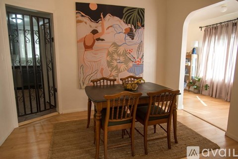 A dining room with a table and chairs and a painting on the wall.
