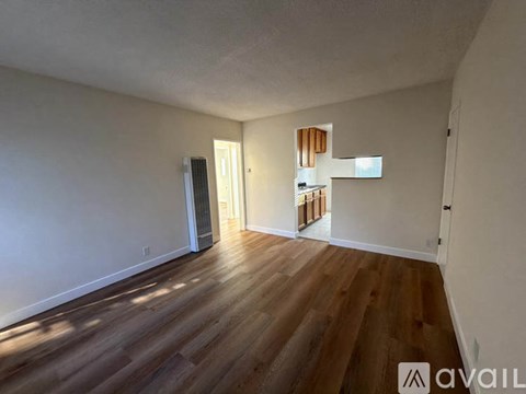 A room with wooden floors and white walls, with a doorway leading to another room.