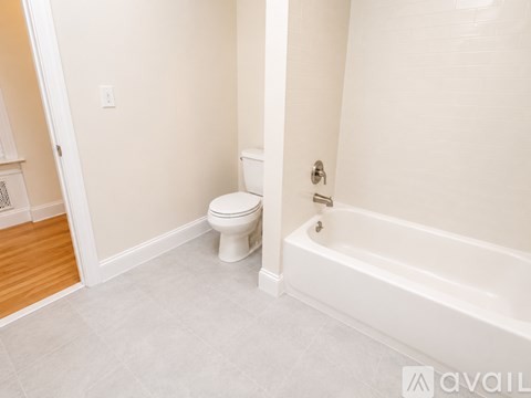 A white toilet sits in a bathroom next to a bathtub.