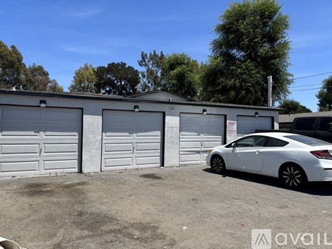 A white car is parked in front of a building with three garage doors.