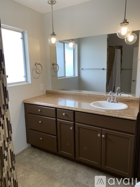 A bathroom with brown cabinets and a round mirror.