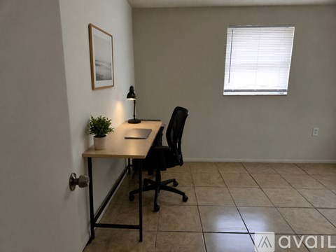 A room with a desk, chair, and a plant.