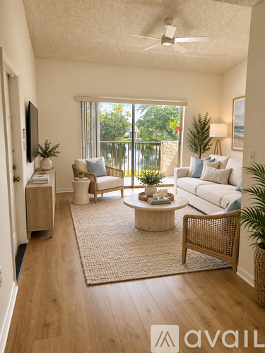 A living room with a white couch, a coffee table, a chair, a plant, and a television.
