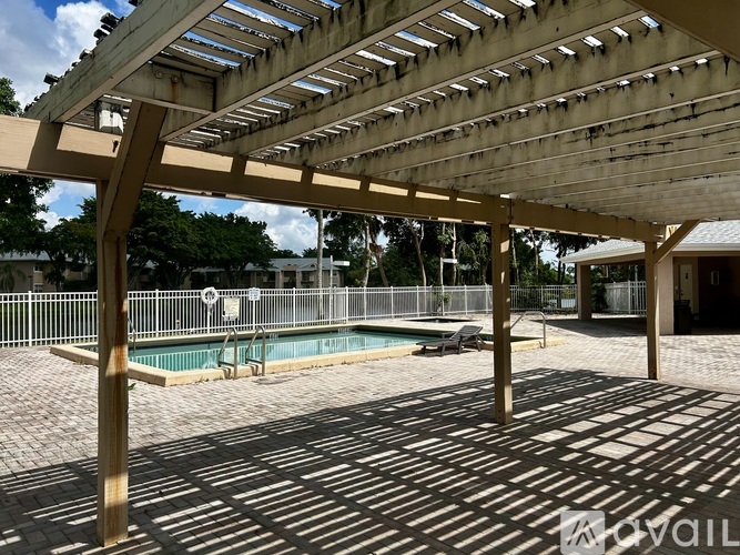 A wooden pergola with a pool in the background.