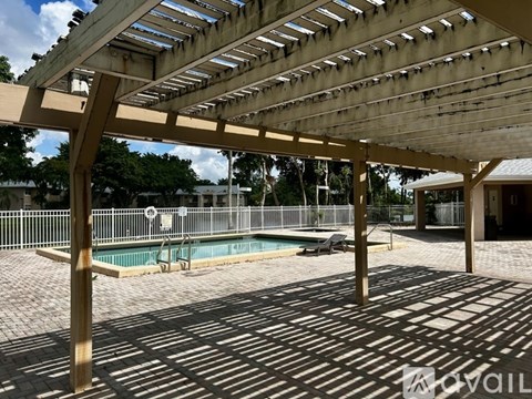 A wooden pergola with a pool in the background.