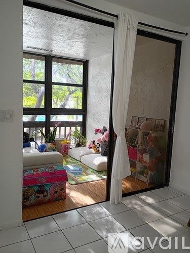 A room with a white couch and a colorful ottoman in front of a sliding glass door.