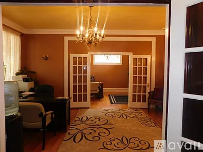 A room with a chandelier, a desk, a chair, and a rug.
