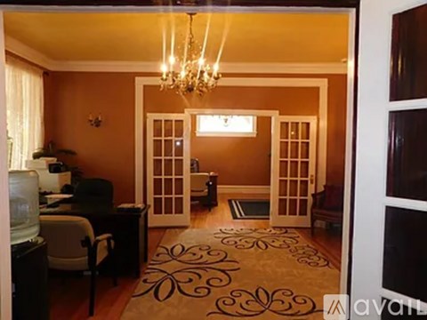 A room with a chandelier, a desk, a chair, and a rug.