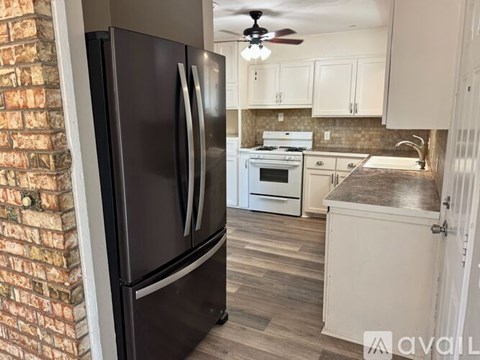 A black refrigerator stands in a kitchen with a brick wall to its left.