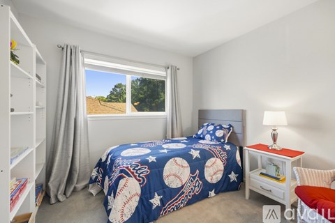 A bedroom with a bed covered in a blue baseball-themed bedspread.