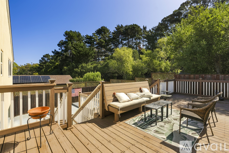 A wooden deck with a sofa and chairs is surrounded by trees.