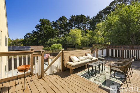 A wooden deck with a sofa and chairs is surrounded by trees.