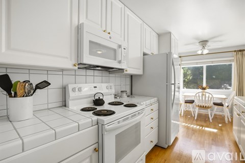 A kitchen with white appliances and cabinets with a window seat.