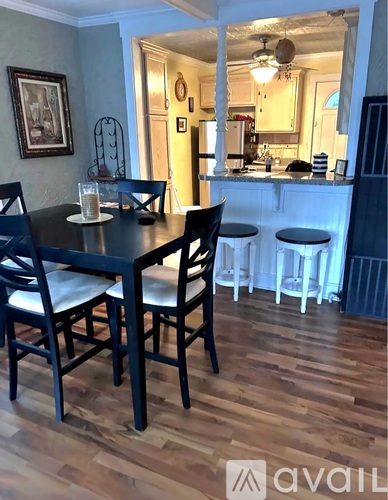 A dining room with a table and chairs and a kitchen in the background.