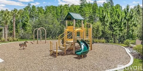 A playground with a green slide and a yellow structure surrounded by trees.