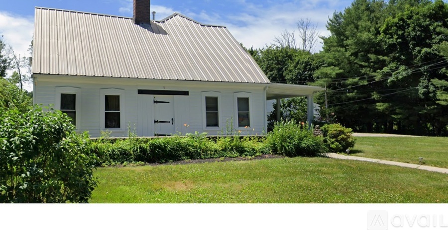 A white house with a grey roof surrounded by greenery.