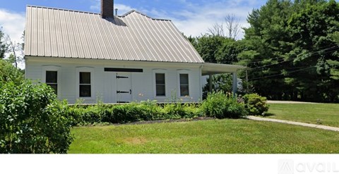 A white house with a grey roof surrounded by greenery.