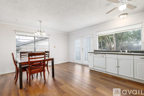 A room with a wooden table and chairs, a ceiling fan, and a window with a view of trees.