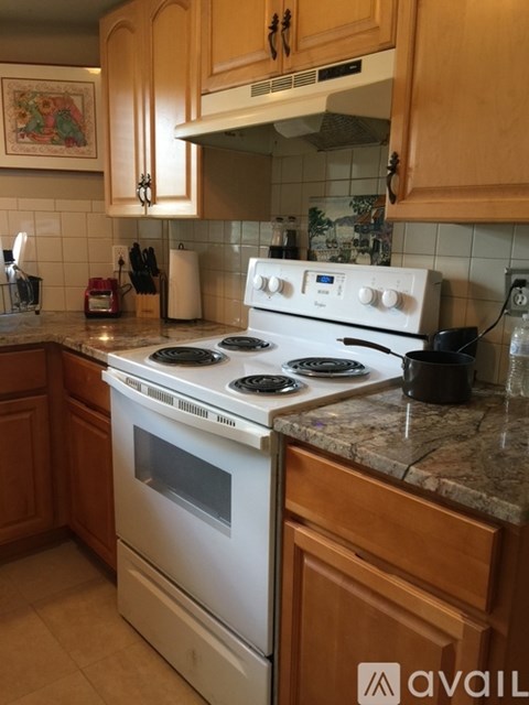 A white stove top oven with four burners and a glass window is in a kitchen with wooden cabinets.