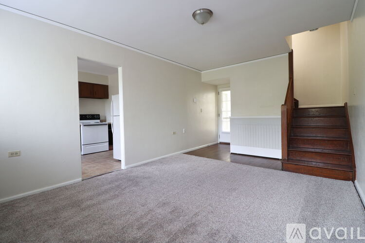 A room with a staircase on the right side and a kitchen area visible through the doorway.