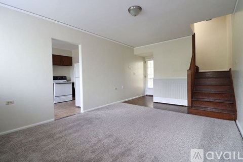 A room with a staircase on the right side and a kitchen area visible through the doorway.