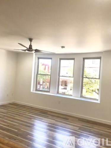 A room with a ceiling fan and three windows.
