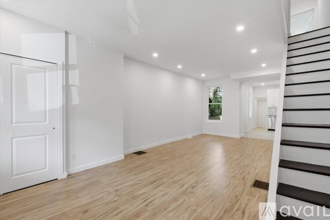 A spacious room with wooden flooring and a staircase on the right side.