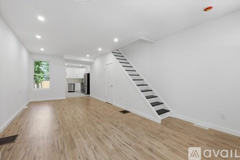A spacious room with wooden flooring and a staircase leading to another room.