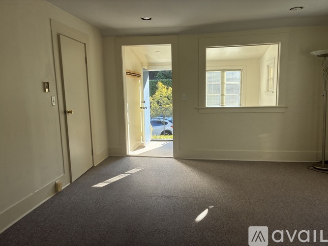 A room with a carpeted floor and a window with a view of trees and a parking lot.