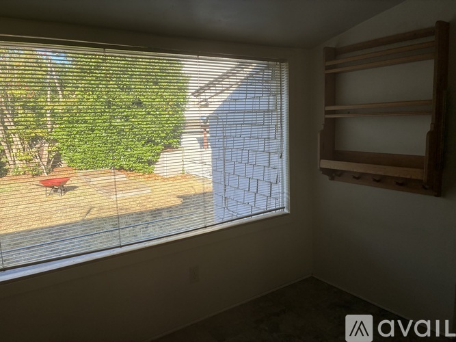 A room with a window covered in blinds, showing a patio with a table and chairs.