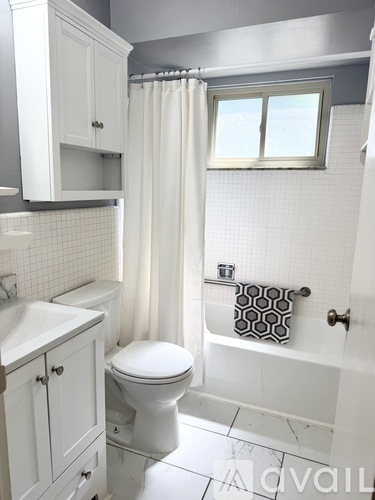 A white toilet sits in a bathroom with white tile floors and white cabinets.