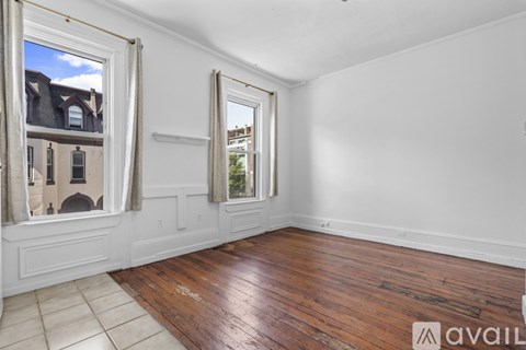 A room with wooden floors and two windows with curtains.
