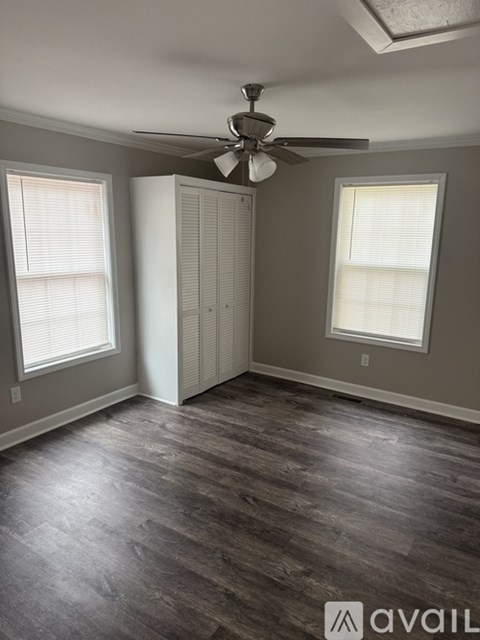 A room with a ceiling fan and two windows.