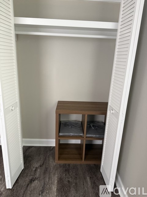 A small wooden table with two shelves is in a corner of a room with white walls.