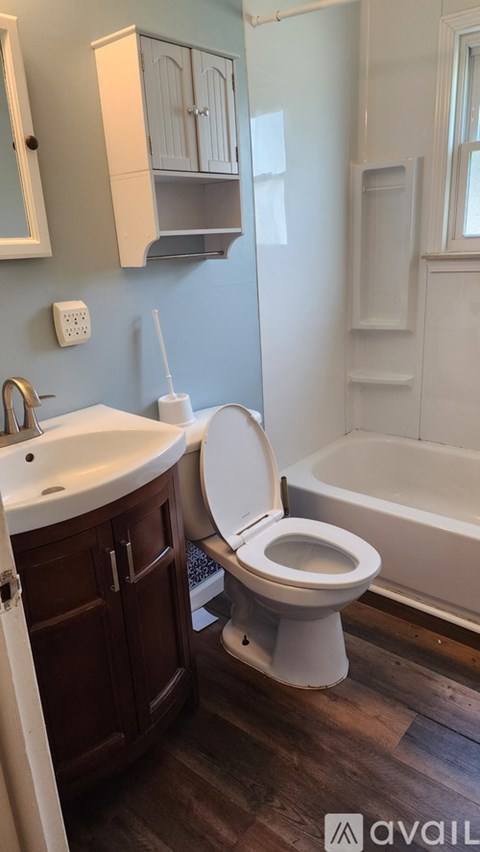 A white toilet is in a bathroom with a white tub and sink.