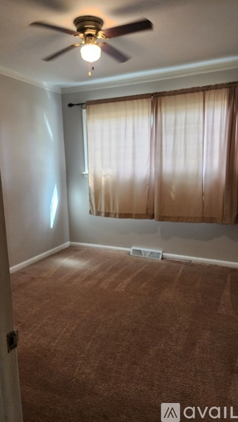 A room with a ceiling fan and a window with curtains.