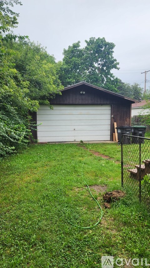A shed with a white garage door is surrounded by greenery.