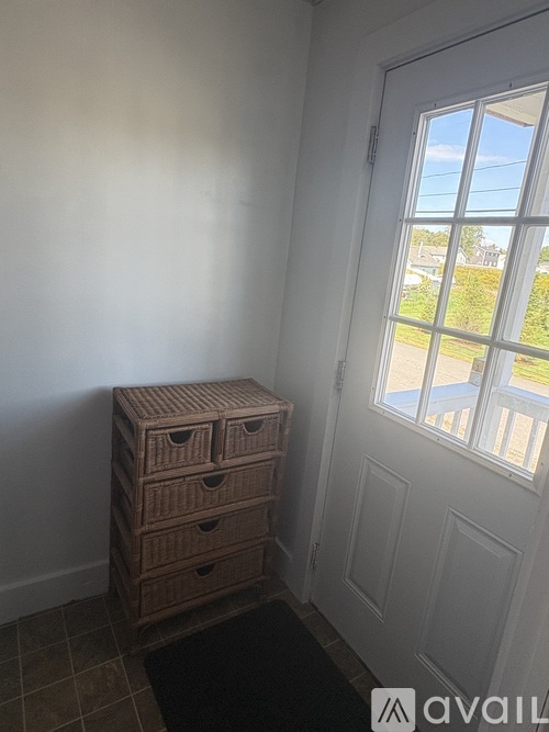 A brown chest of drawers sits in front of a white door with a window showing a view of a street.