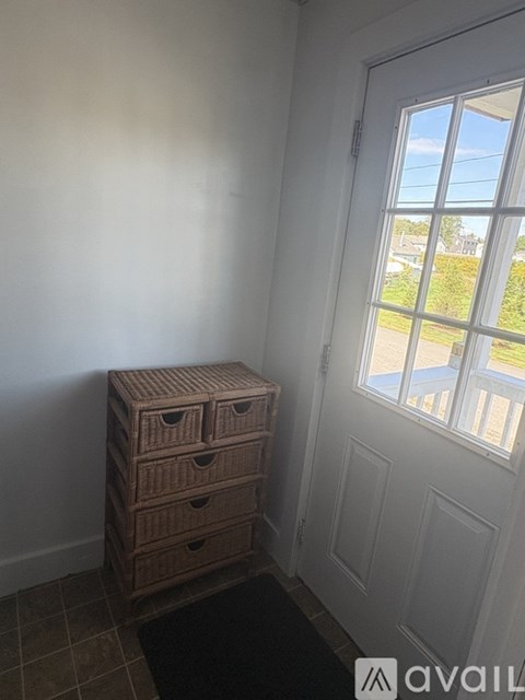 A brown chest of drawers sits in front of a white door with a window showing a view of a street.