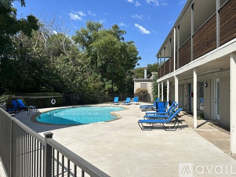 A pool surrounded by blue lounge chairs and a white fence.