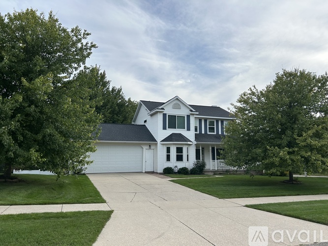 A white house with a grey roof and a driveway in front.
