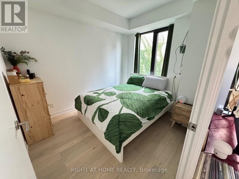 A bedroom with a bed, nightstand, and a plant.