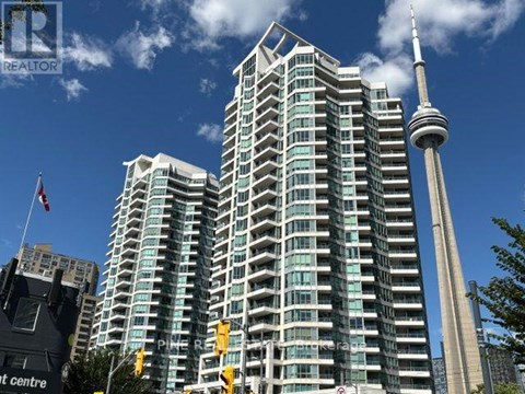 A tall building with a glass facade stands next to a tall tower with a spire.