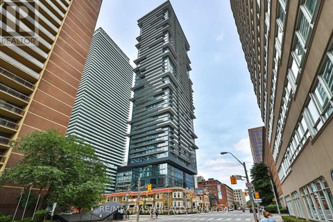 A tall building with a glass facade stands in the middle of a city street.