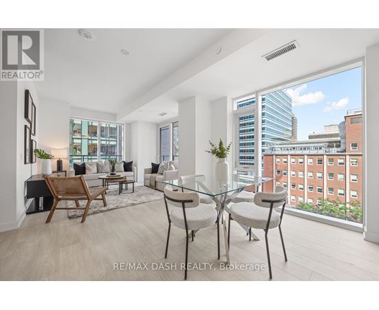 A well-lit, modern living room with a glass table and chairs, a wooden chair, and a view of a cityscape through the window.