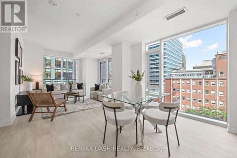 A well-lit, modern living room with a glass table and chairs, a wooden chair, and a view of a cityscape through the window.
