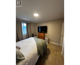 A bedroom with a bed, a window with curtains, a dresser with a flat screen TV mounted above it, and a white wall.
