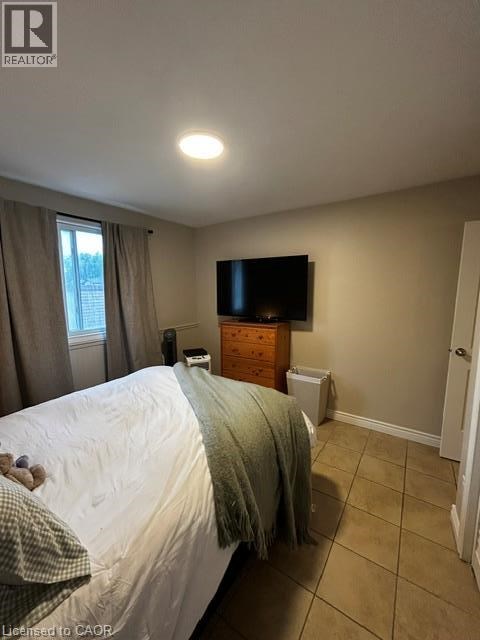 A bedroom with a bed, a window with curtains, a dresser with a flat screen TV mounted above it, and a white wall.